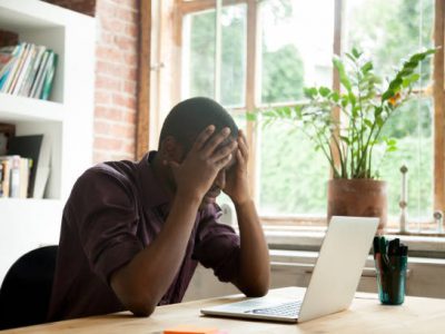 A man sitting at a desk, visibly distressed, with his head resting in his hands, deep in thought.